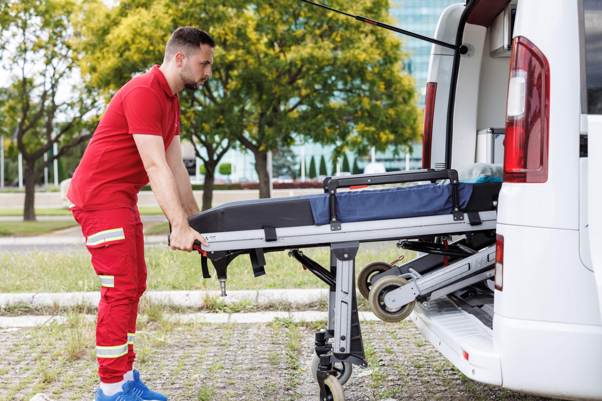 Mentőszolgálat munkatársai fekvő beteget emelnek be hordágyon egy betegszállító autóba ambuláns betegszállítás során